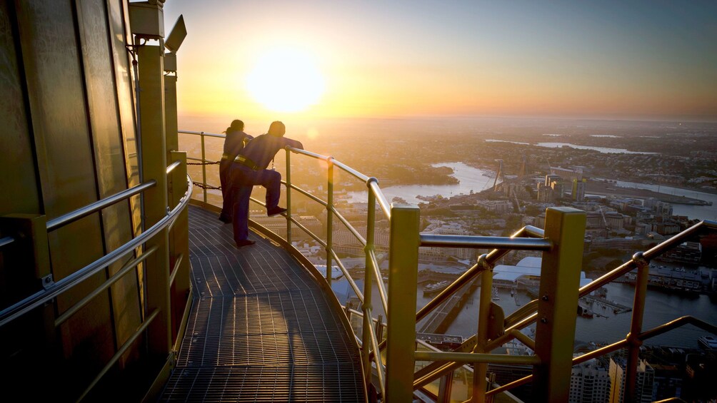 Guests on the Skywalk at the Sydney Tower Eye take a break standing on a platform overlooking the city in Sydney as the sun is setting