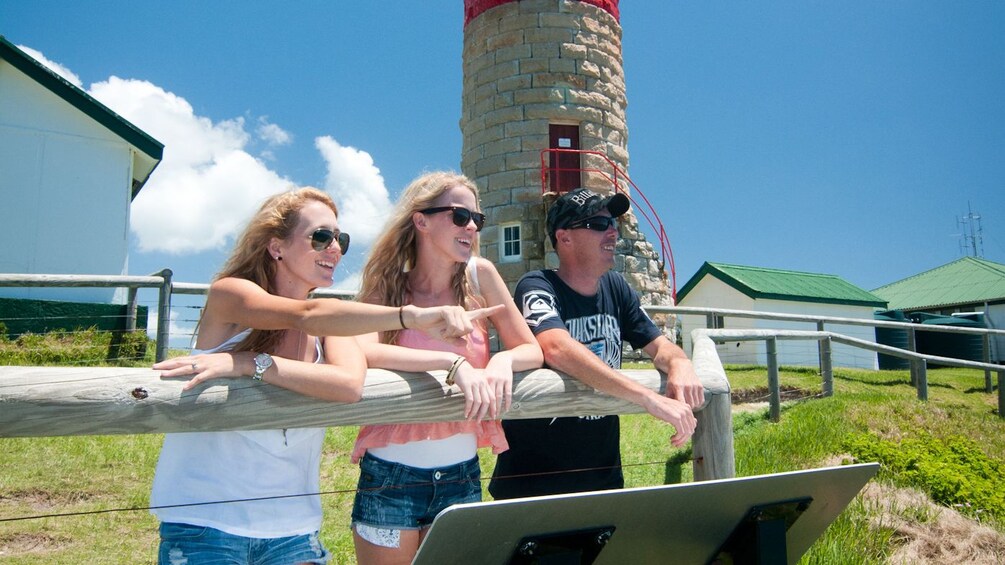 three people lean on fence by lighthouse in Brisbane