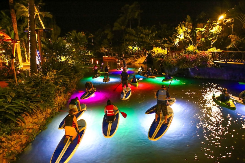 Colorfully illuminated pool at night with paddleboarders