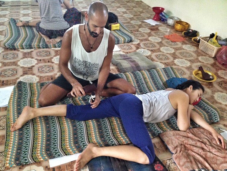 Man uses wooden tool on partner's leg during Thai massage
