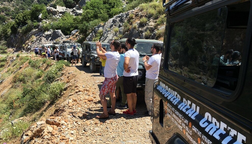 Tourists take photos of view near line of Land Rovers in Crete, Greece