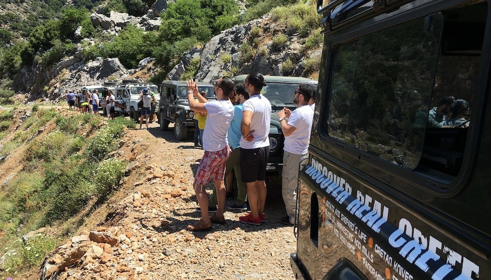 Tourists take photos of view near line of Land Rovers in Crete, Greece