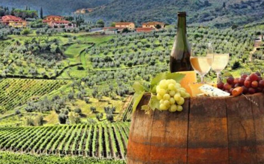 Wine, cheese and grapes on wine barrel in front of vineyards
