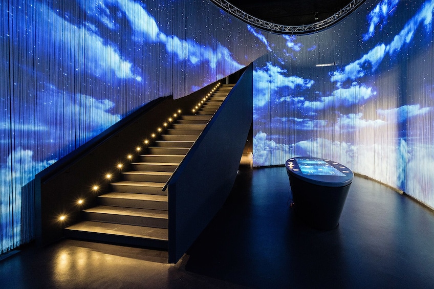 Dark room with lit staircase and projected clouds on walls