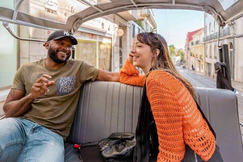 Tourists enjoying a tuk tuk guided tour in Lisbon on a sunny day.