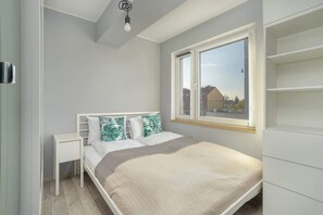 A cozy bedroom featuring a double bed with white linens, leafy pillows, and a built-in wardrobe under natural light.
