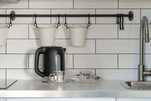 A modern kitchen detail: white subway tiles, a black kettle on the counter, and two mugs hanging on a rail.
