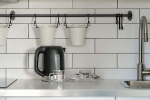 A modern kitchen detail: white subway tiles, a black kettle on the counter, and two mugs hanging on a rail.