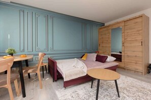A comfortable seating and dining space showcasing pastel-blue paneling, a burgundy sofa, and light-gray flooring, blending modern and classic elements.
