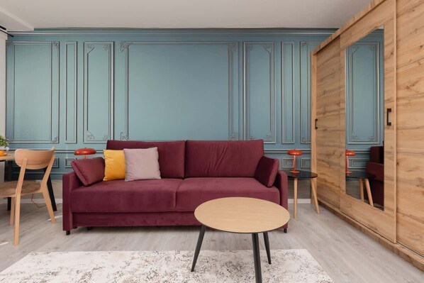 A bright and cozy living area with pastel-blue paneled walls, a burgundy sofa, and a round wooden coffee table, creating a warm atmosphere.
