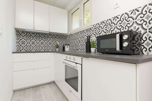 A modern white kitchen with black-and-white patterned tiles, sleek cabinets, and small appliances on a dark countertop, offering both style and functionality.
