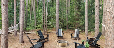 6 Adirondack chairs surround the fire pit with string lights hung around.