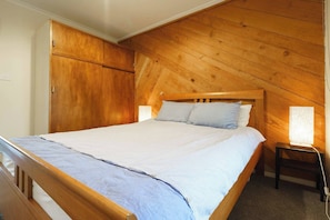  The main bedroom features a comfy queen-size bed surrounded by rustic timber walls.
