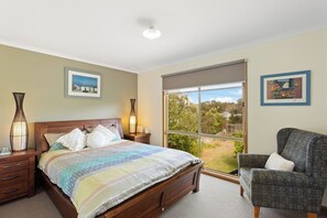  The first bedroom features a timber queen-sized bed, a reading chair and a lush leafy outlook.
