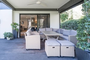 The alfresco dining area has a wrap around cushioned wicker lounge and armchairs with a long table. Enjoy meals together comfortably under cover with ambient lighting and a cool fan breeze. 