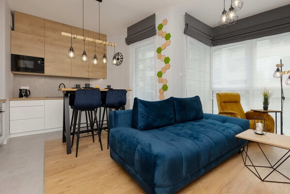 A modern living room featuring a blue velvet sofa, a black coffee table, and stylish wall decor, creating a cozy yet elegant space.
