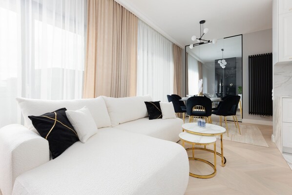 A modern living room featuring a white sectional sofa, a glass coffee table, and beige curtains creating a luxurious ambiance.

