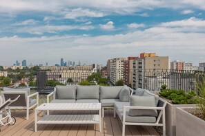 A balcony with outdoor seating offering views of the city skyline and green surroundings.

