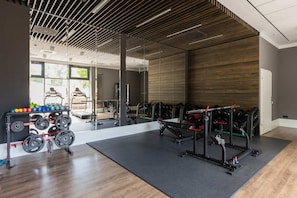A gym with various fitness equipment, set against wooden accents and large glass walls.

