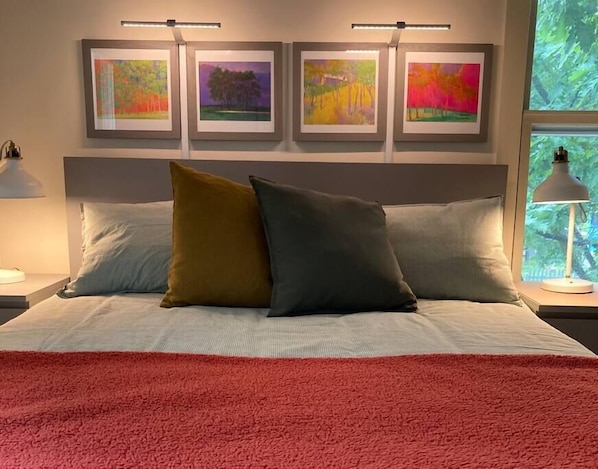 Queen bed in first bedroom with colorful Wolf Kahn prints overhead.