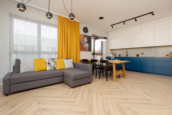 A modern living room with gray and blue furniture, including a sofa and a dining table, accented by a mustard-yellow curtain that brings a pop of color into the space.