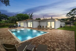 Private backyard with pool, hot tub, sun shelf, loungers, dining area, & grill.