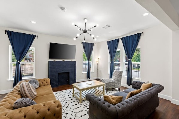 As you step inside, you're greeted by a seamless blend of sophistication and coziness, large windows dressed in flowing curtains frame the space, allowing natural light to flood in during the day and framing views of the outside world.