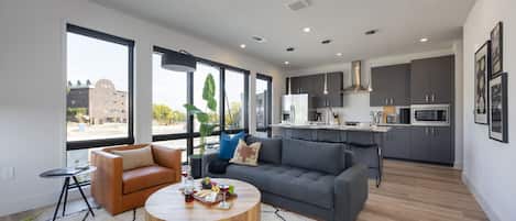 Modern open concept living area with floor to ceiling windows, designer furniture, smart TV, and access to private patio.