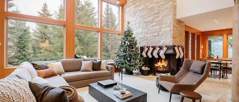 The open-plan living area features vaulted ceilings and a grand stone fireplace, creating the perfect ambiance for relaxation and gatherings, decorated for holidays