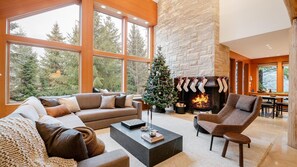 The open-plan living area features vaulted ceilings and a grand stone fireplace, creating the perfect ambiance for relaxation and gatherings, decorated for holidays