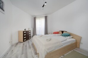 A cozy bedroom with a duble bed, colorful pillows, and a wooden dresser near the window.
