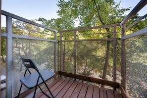 A spacious balcony with a wooden floor, black railing, and outdoor furniture, offering a relaxing view of greenery.
