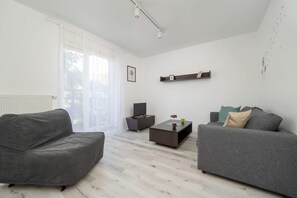 A bright living room with a grey sofa, a coffee table, and minimalist shelving on the walls, providing a functional and stylish space.
