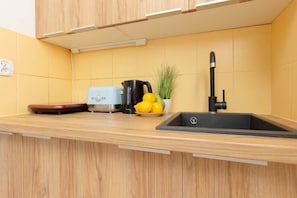 A modern kitchenette with wooden cabinets, a black sink, and small appliances, designed in a warm and functional style.