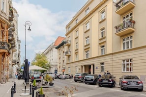 A street view outside the apartment, showcasing a charming building facade, parked cars, and tree-lined sidewalks.
