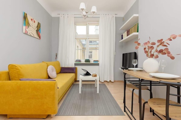 A cozy living room featuring a yellow sofa, a white coffee table, and a bright window with sheer curtains letting in natural light.