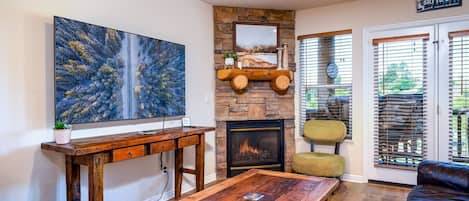 Experience the cozy living room, outfitted with plush seating, a fireplace, an expansive smart TV, and patio doors that frame the breathtaking mountain vistas.
