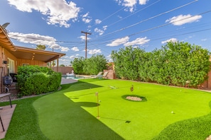 Backyard accessible from the kitchen with ample outdoor seating, pool, and putting green.