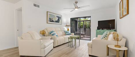 Beautifully decorated living room is equipped with a smart TV, a comfy leather sofa sleeper, a loveseat, a cozy chair, and sliders to a screened patio.