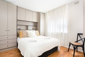 A stylish bedroom is furnished with a plush queen bed, luxurious black-out blinds and ample built-in cupboard space.