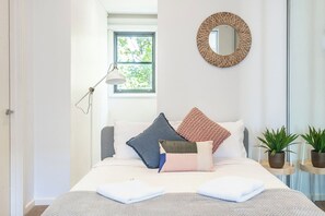In the bedroom, a queen sized bed is topped with plush furnishings with a reading light and storage.