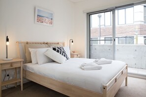 The queen bedroom features hotel-style premium linens and full-length windows allowing for natural light to stream in.