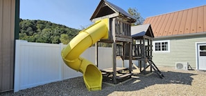 Kids will love this wooden playset featuring a bright yellow slide and a built-in, kid-sized picnic table. Conveniently located in the backyard, it offers a perfect space for fun with beautiful hillside views.