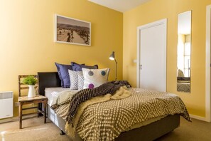 The first bedroom boasts bright yellow walls and a comfortable queen bed.