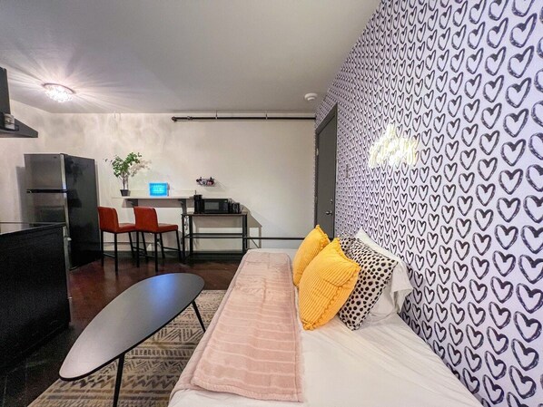 Immerse yourself in a visual delight in our luxurious living space, featuring rich purple heart wallpaper, plush cushions, and a striking oval table. Experience the perfect blend of comfort and style, with a fully stocked fridge and a sleek oven adding a touch of practicality to this opulent setting.