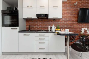 A modern kitchen with white cabinetry, a black countertop, and a striking brick accent wall for contrast.
