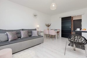 A spacious living room with a grey sectional sofa, a small dining table, and a bright, airy ambiance.
