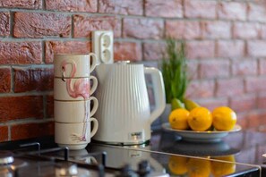 A close-up of a kitchen countertop with stacked mugs, a jug, and fresh lemons on a reflective tray.
