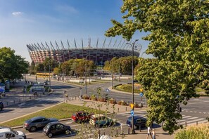 A view from a window, showing a Stadion Narodowy in Warsaw and some greenery outside. The picture provides a glimpse of the surroundings from the apartment.
