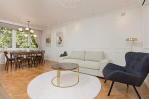 Another view of the living room, showing a spacious seating area with a white sectional sofa and a small black armchair. The room has a contemporary design.